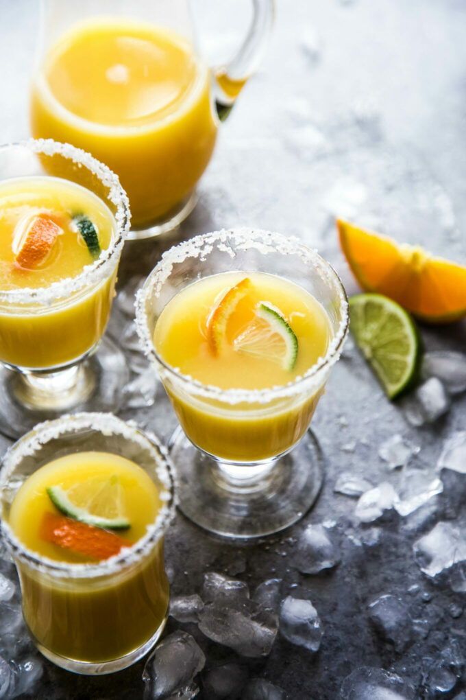 three glasses filled with orange juice and garnished with limes on the side