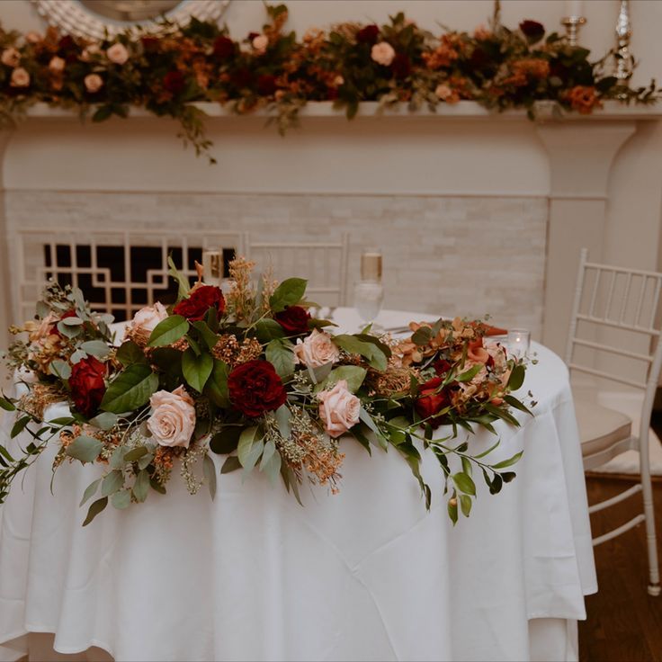 a table with flowers and greenery on it in front of a fire place mantle