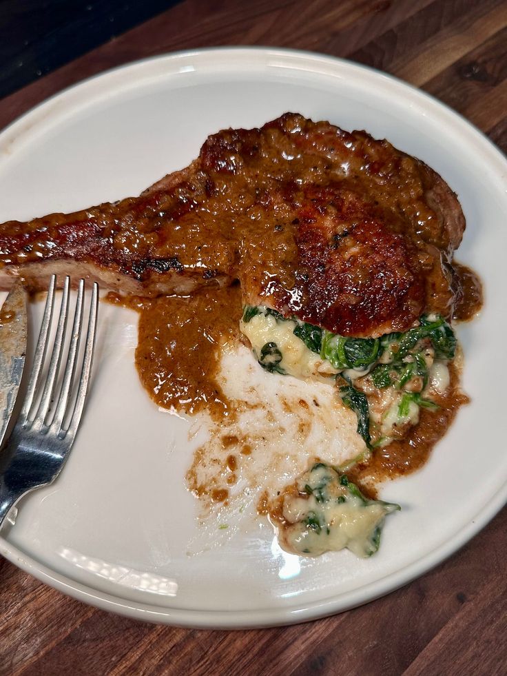 a white plate topped with meat and gravy next to a knife and fork