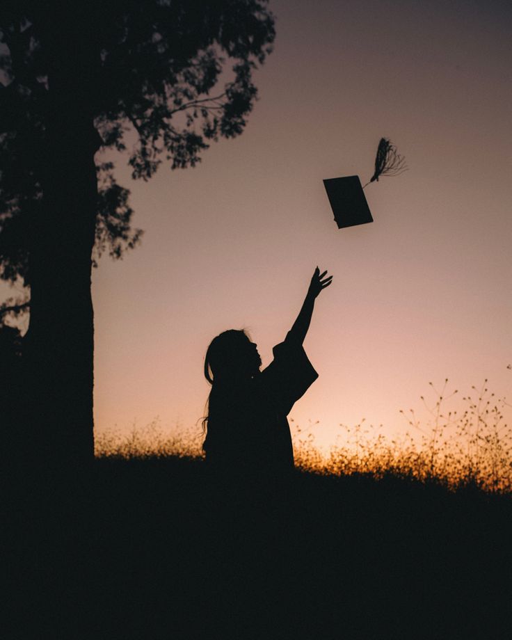 a woman flying a kite in the air at sunset or dawn with her hands up