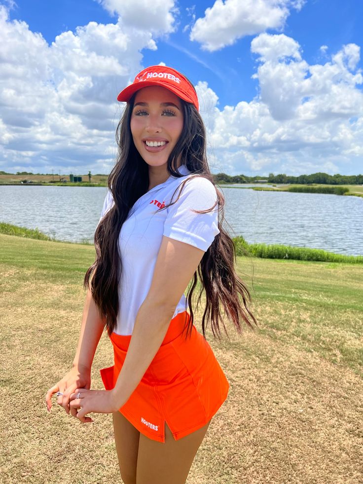 a woman in an orange skirt and white shirt posing for a photo by the water