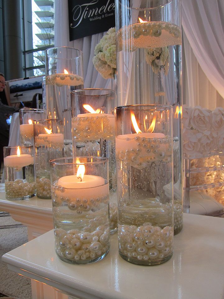 several tall vases filled with white flowers and lit candles