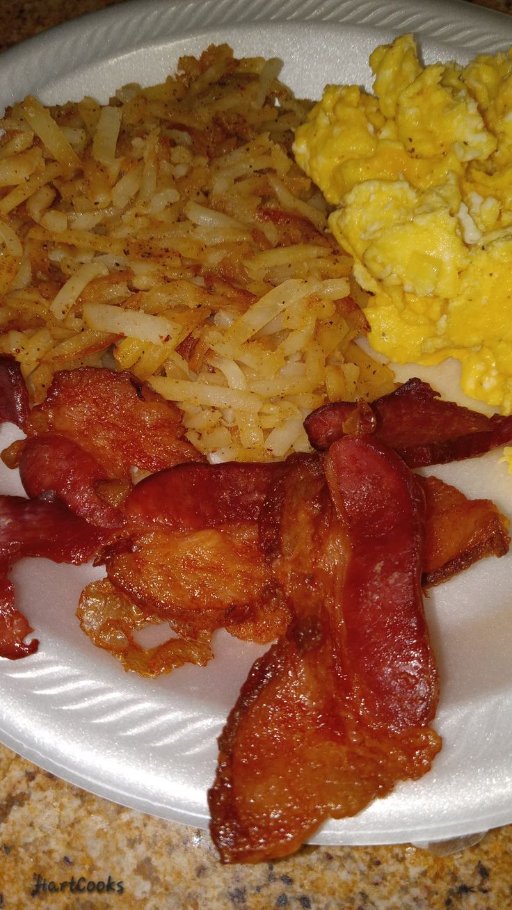 a white plate topped with bacon, eggs and hash browns on top of a counter