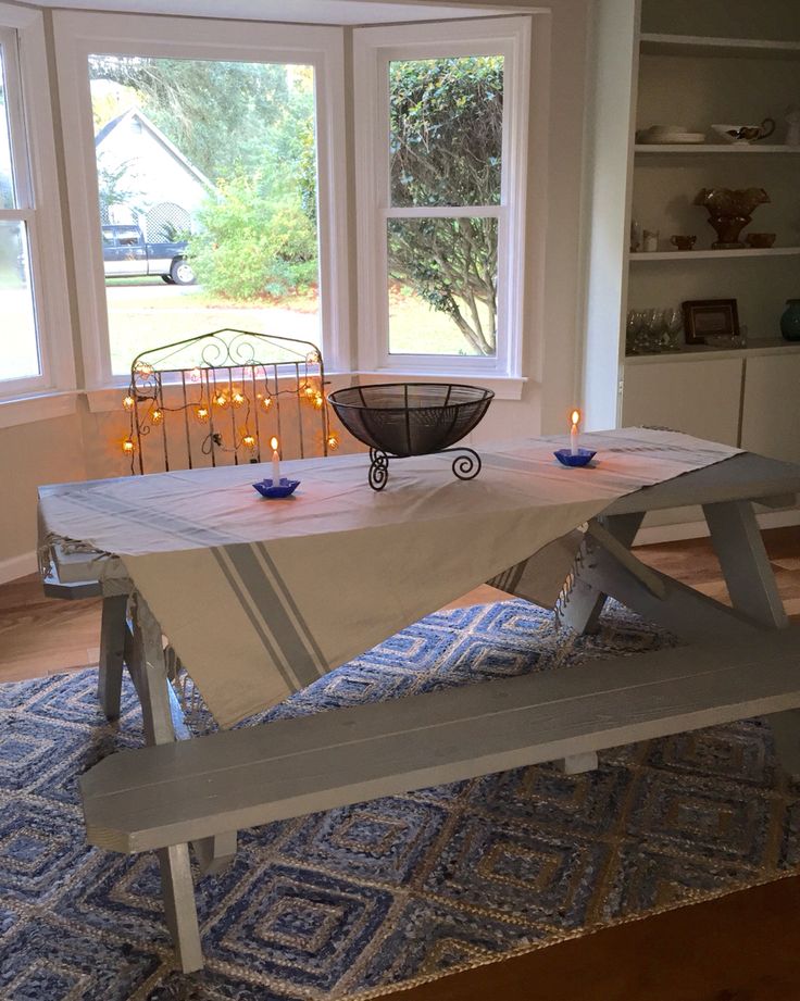 a white table with candles on it in front of two windows and a blue rug