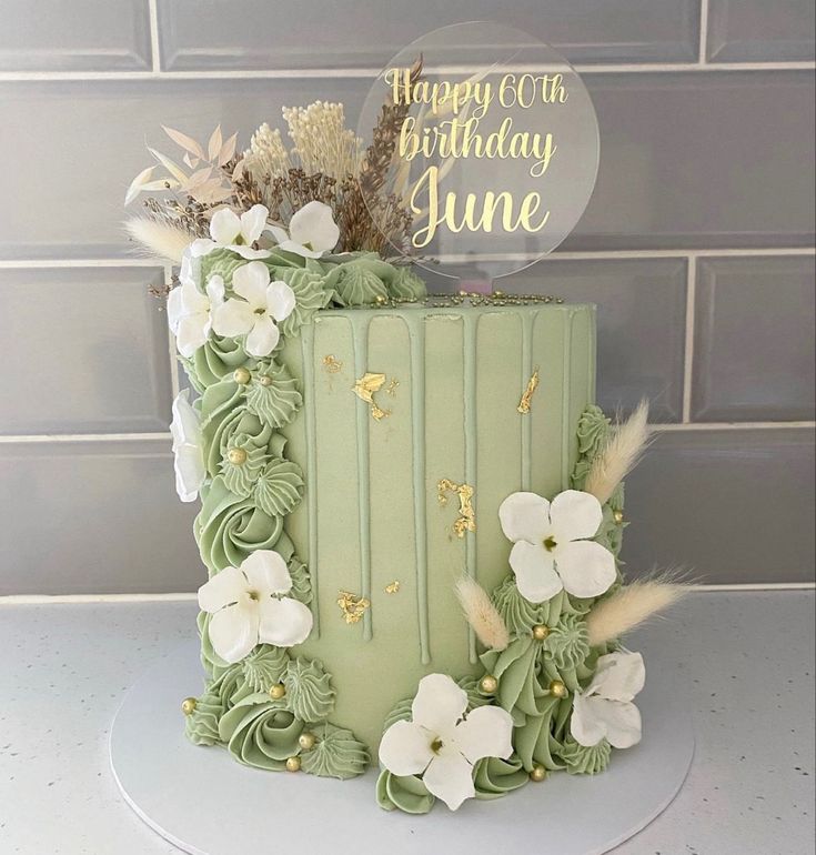 a green cake with white flowers and gold lettering on top is sitting on a table