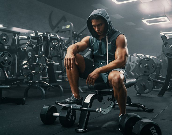 a man sitting on top of a bench in a gym filled with dumbbells