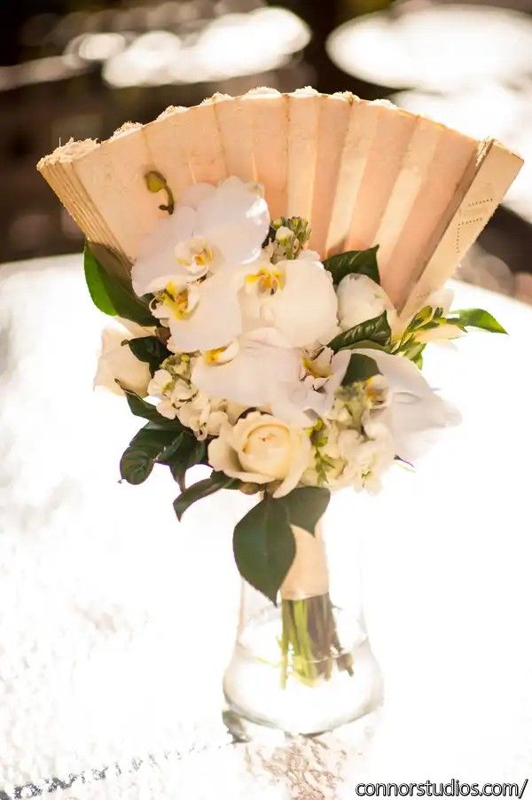 a bouquet of white flowers in a vase on a table with an open fan as the centerpiece