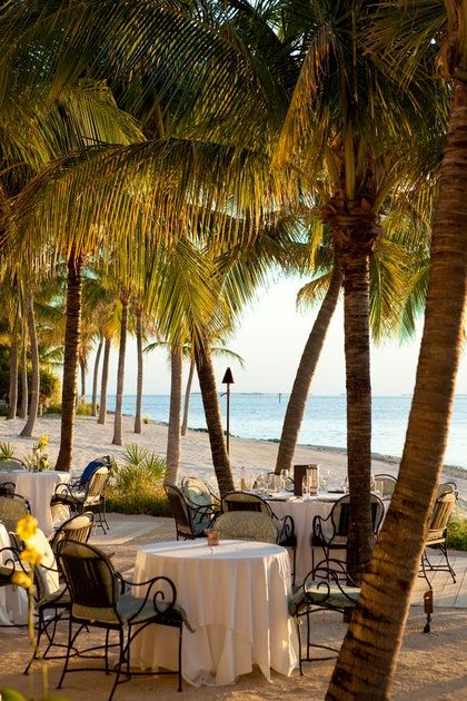 tables and chairs are set up on the beach with palm trees in front of them