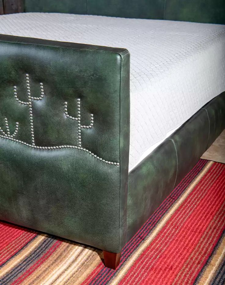 a green leather bed frame with cactus embroidered on the top and bottom, sitting on a striped rug