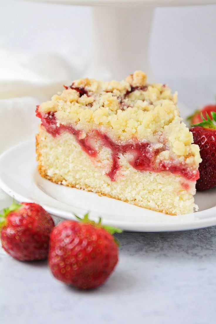 a slice of strawberry crumb cake on a white plate with strawberries around it