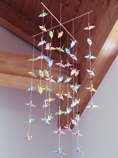 a wind chime hanging from the ceiling with paper cranes on it's strings