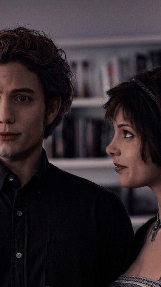 two people standing next to each other in front of a book shelf with books on it