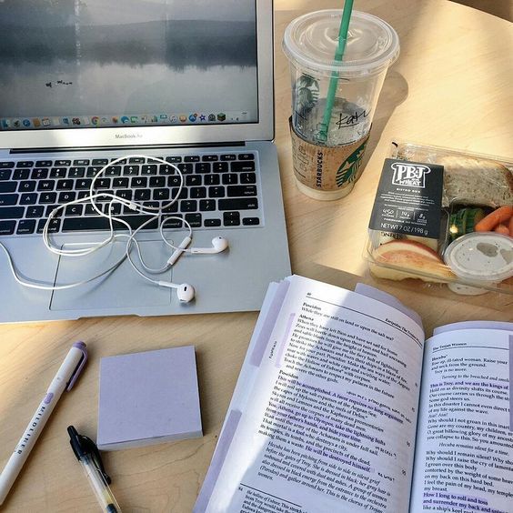 an open book sitting on top of a wooden table next to a laptop computer and cup of coffee