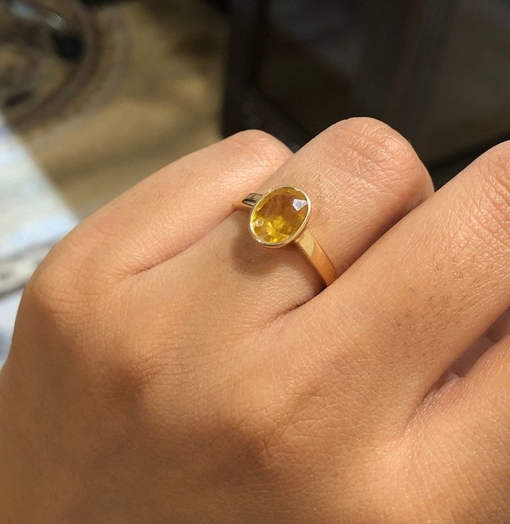 a woman's hand holding a yellow ring with a stone in the middle,