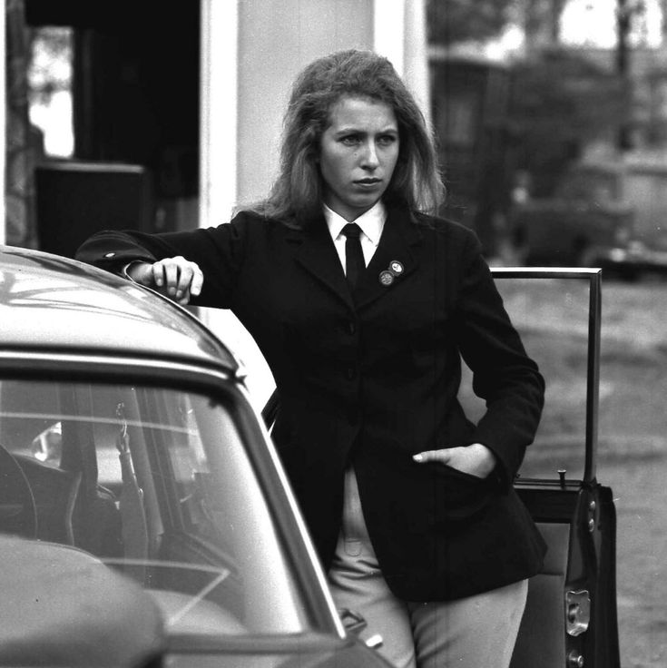 a woman standing next to a car with her hand on the door handle and looking at the camera