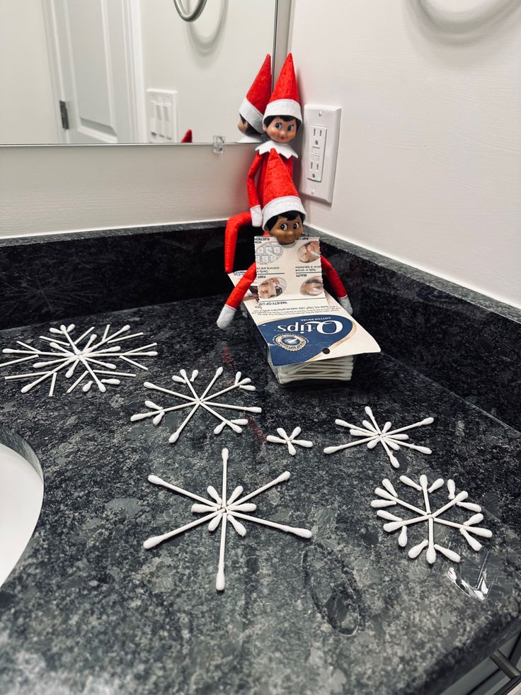 an elf is sitting on top of a box in the bathroom with snowflakes