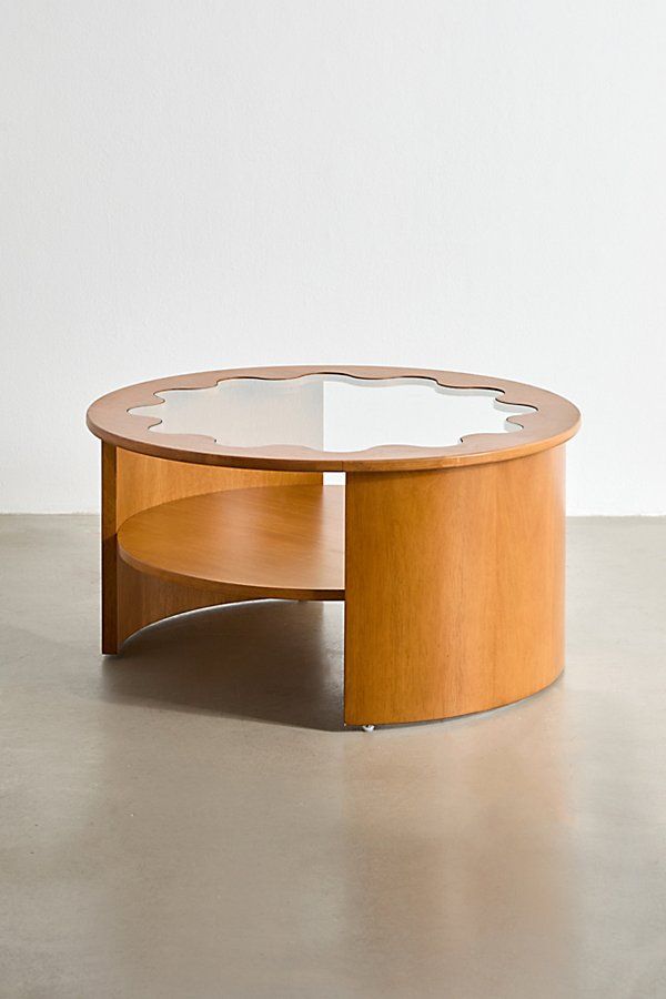 an oval coffee table with glass top and wooden frame, in front of a white wall