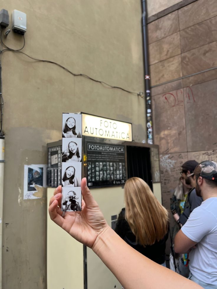 a person holding up a cell phone in front of a wall with pictures on it