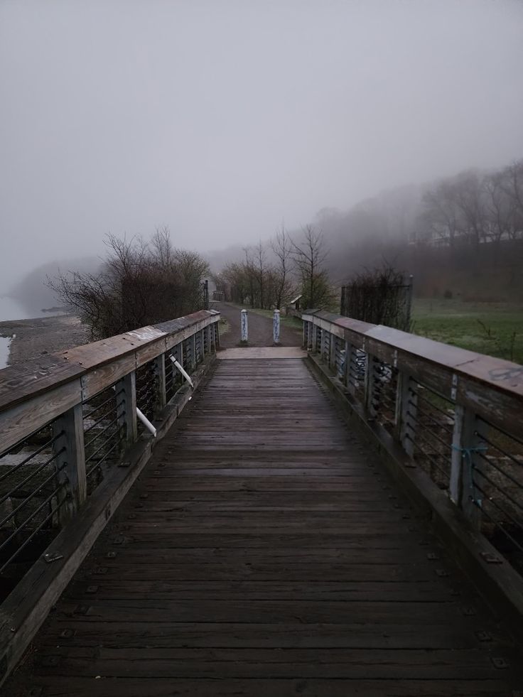 a wooden bridge with railings leading to the water on a foggy, overcast day