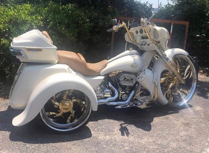 a white motorcycle parked on top of a parking lot next to some bushes and trees