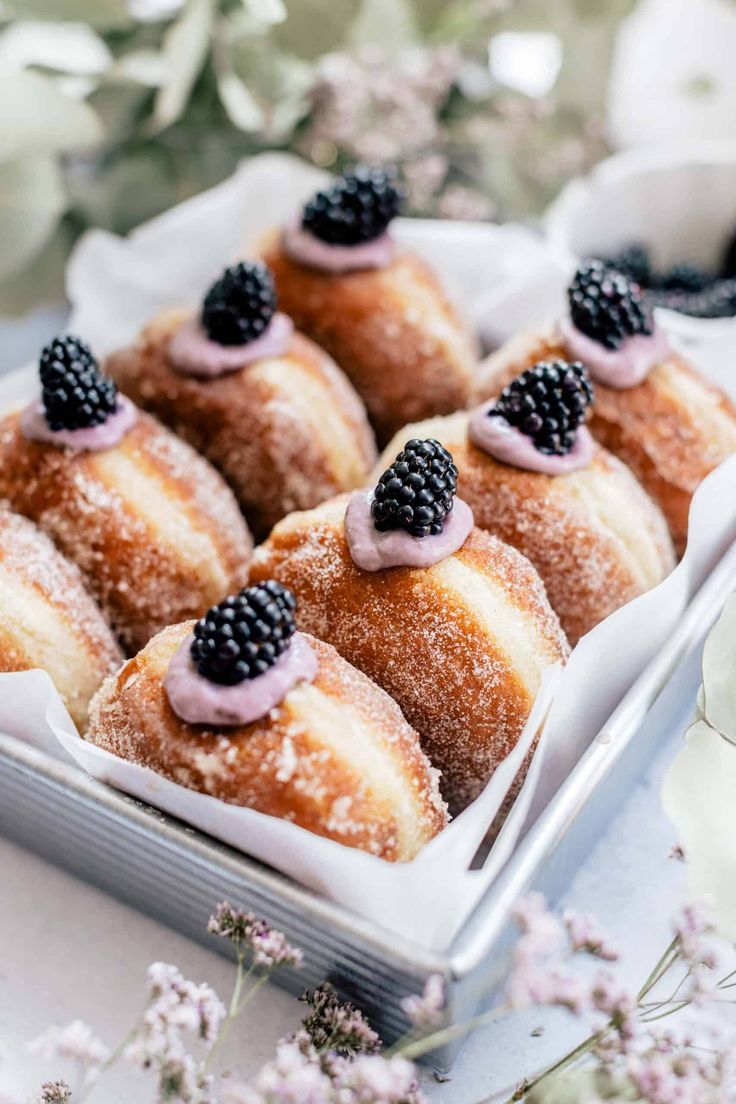 several pastries with blackberries and powdered sugar are in a white box on a table