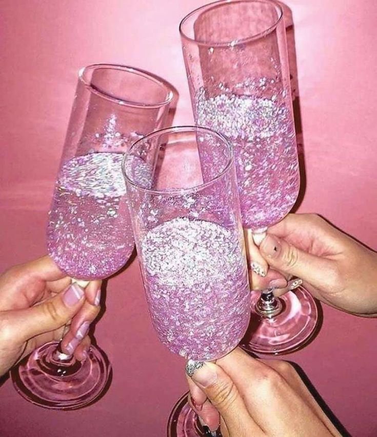 three people are holding up wine glasses with pink liquid in them and glitter on the rims