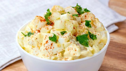 a white bowl filled with potato salad on top of a wooden table next to a napkin