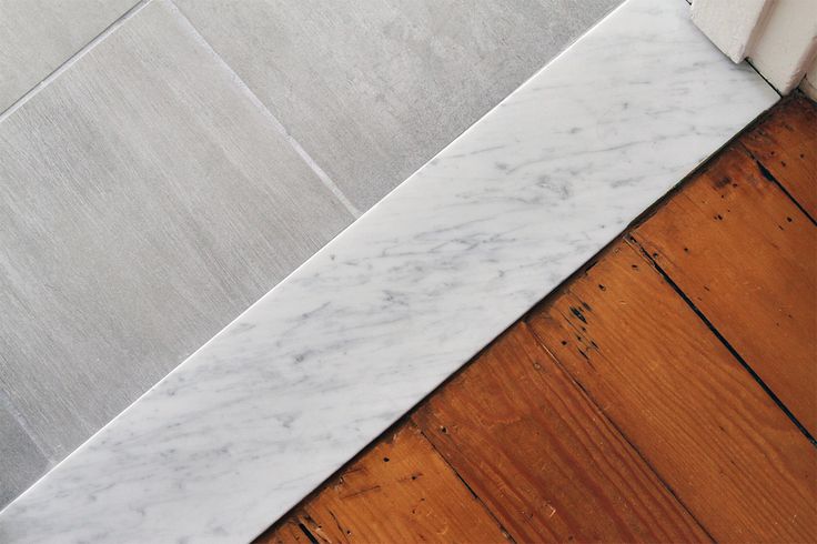 the corner of a bathroom with wood flooring and white marble tiles on the wall