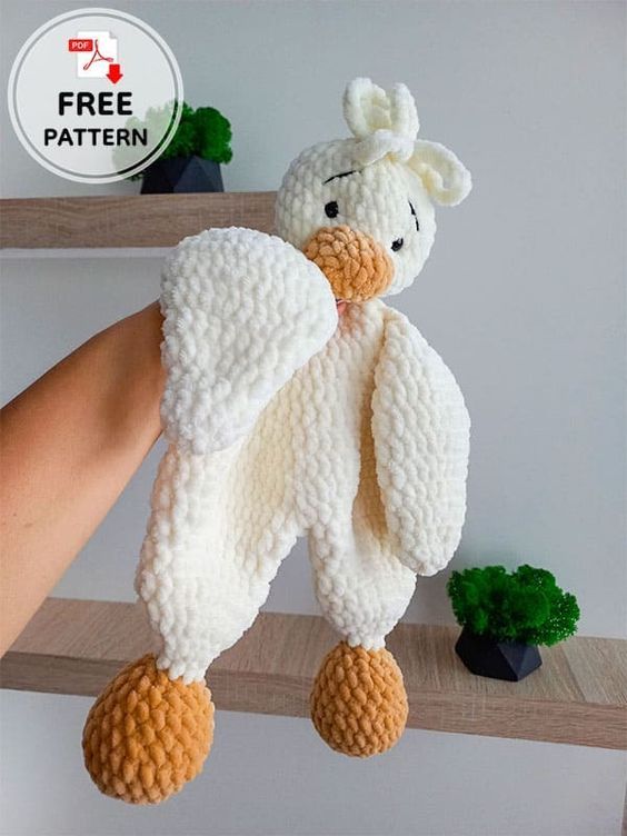 a hand holding a knitted stuffed animal in the shape of a duck on a shelf