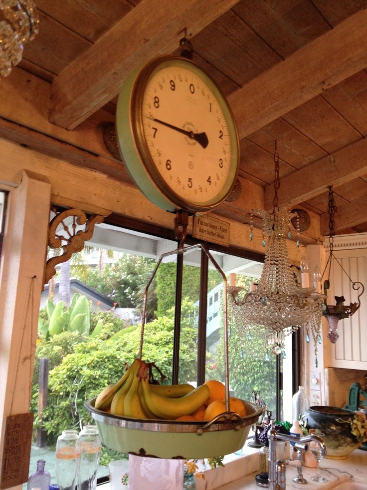 a clock hanging from the ceiling in a kitchen with bananas and chandelier on it