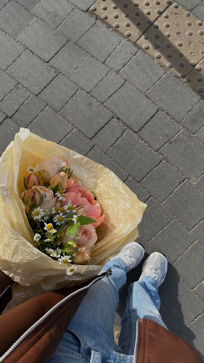 someone is holding a bouquet of flowers in their hand while sitting on the ground outside