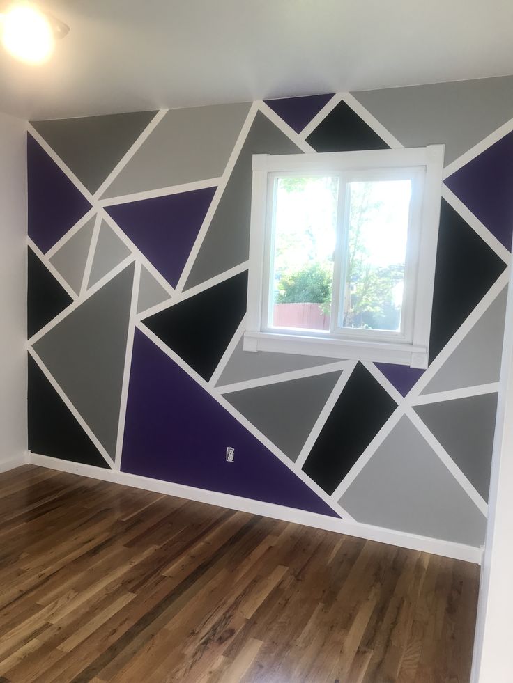 an empty room with wood flooring and painted geometric designs on the wall behind it