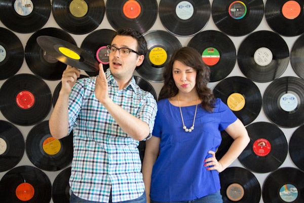 a man and woman standing next to each other in front of record records on the wall