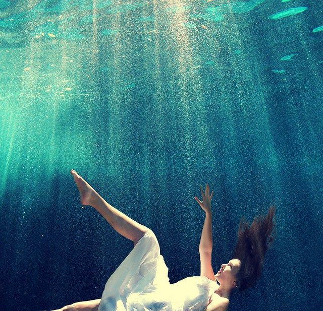 a woman is floating in the water with her arms up and legs spread out,