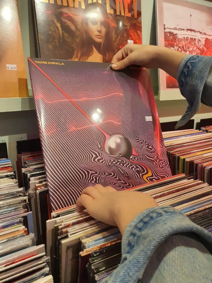 a person holding up a cd case in front of a wall full of record records