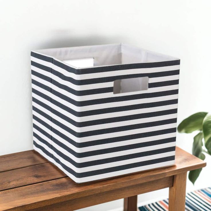 a black and white striped storage bin sitting on top of a wooden table next to a potted plant