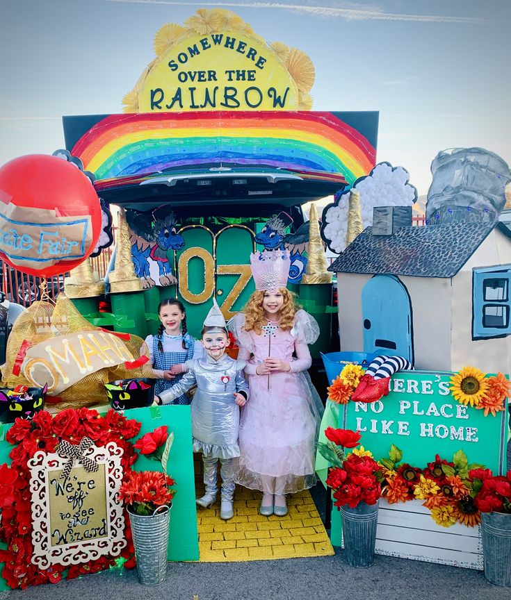 two children standing in front of a fake rainbow ride at an amusement park with balloons and decorations