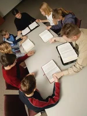 a group of people sitting around a table with open books in front of them on top of each other