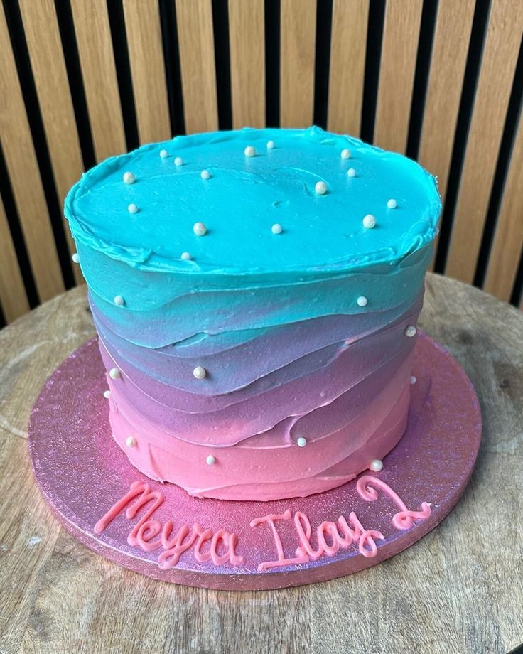 a cake that is sitting on top of a wooden table with the words happy birthday written in pink and blue frosting