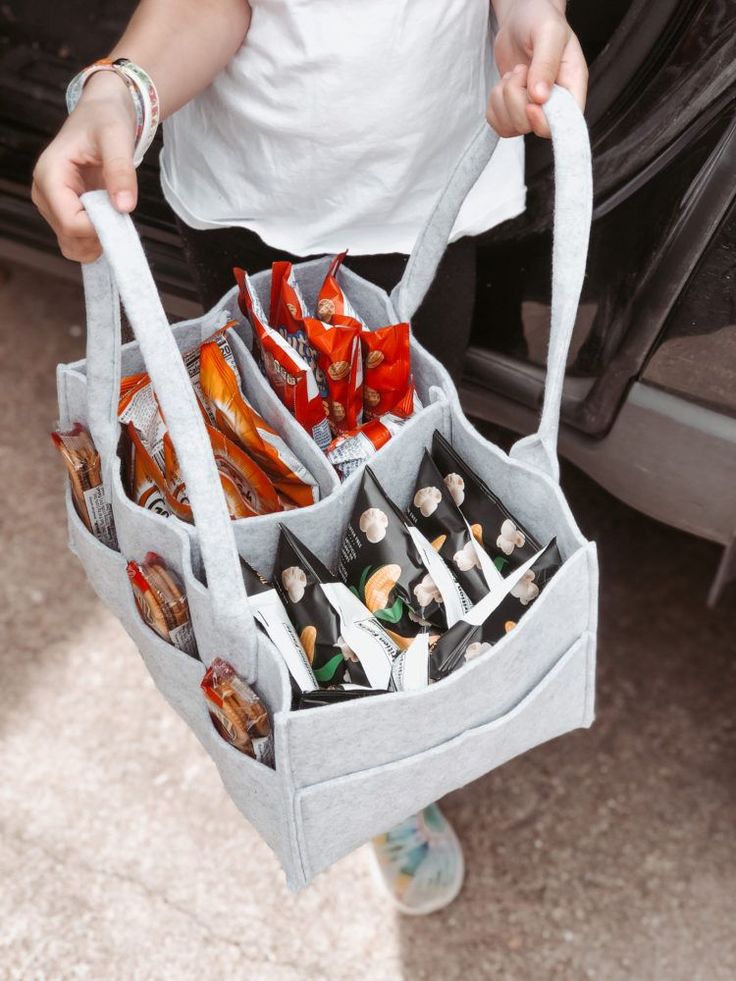 a person holding a gray bag filled with candy and candies in front of a car