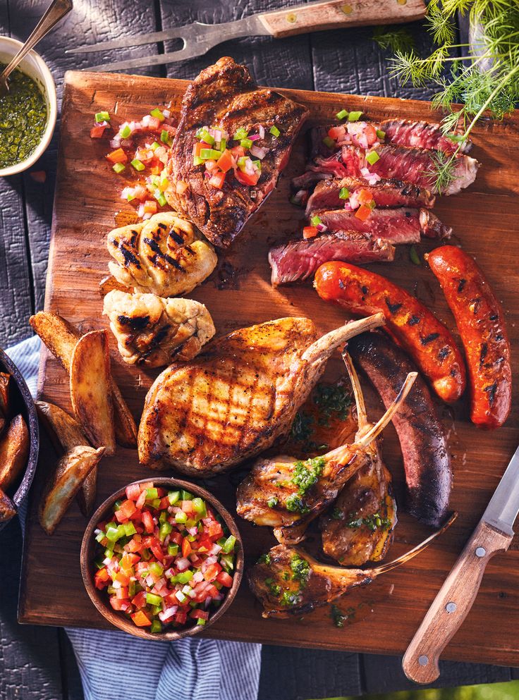 steaks, potatoes and vegetables on a cutting board next to a bowl of salsa