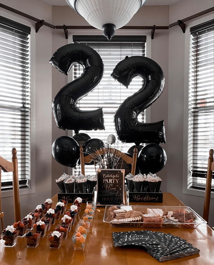 the table is set up with black balloons and desserts