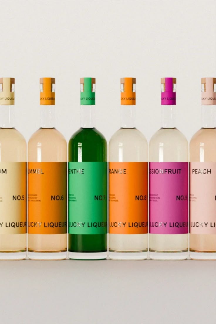 six bottles of liquid are lined up in a row on a white surface, each containing different colored labels