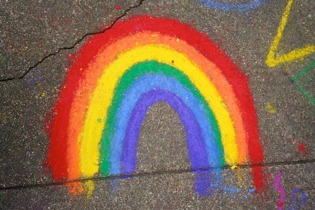 a rainbow painted on the sidewalk with chalk paste and crayons next to it