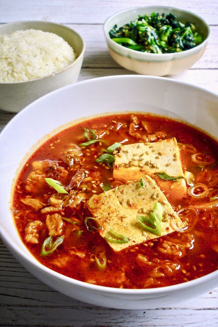 a bowl of soup with tofu, rice and broccoli on the side