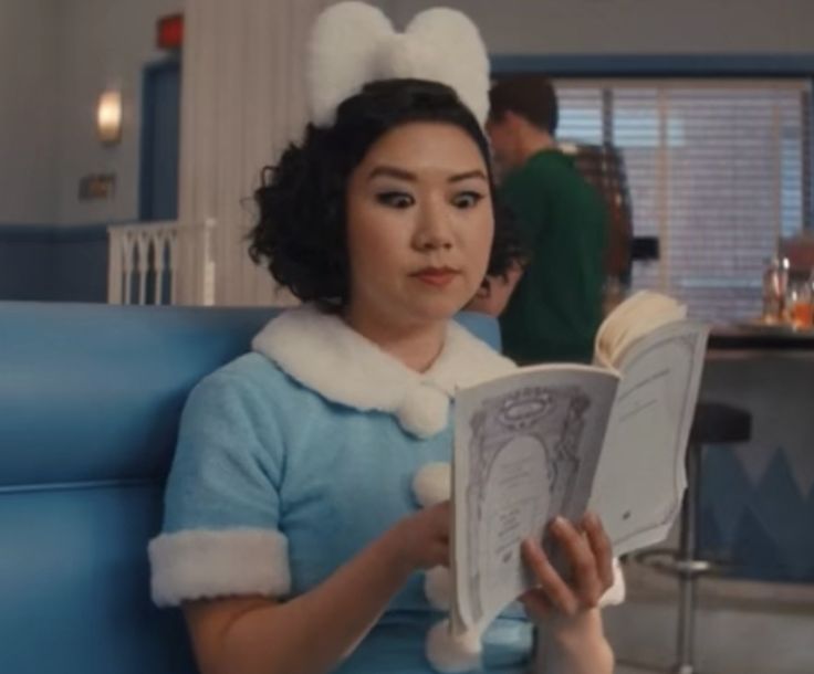 a woman sitting on a blue couch reading a book while wearing a bunny ears hat