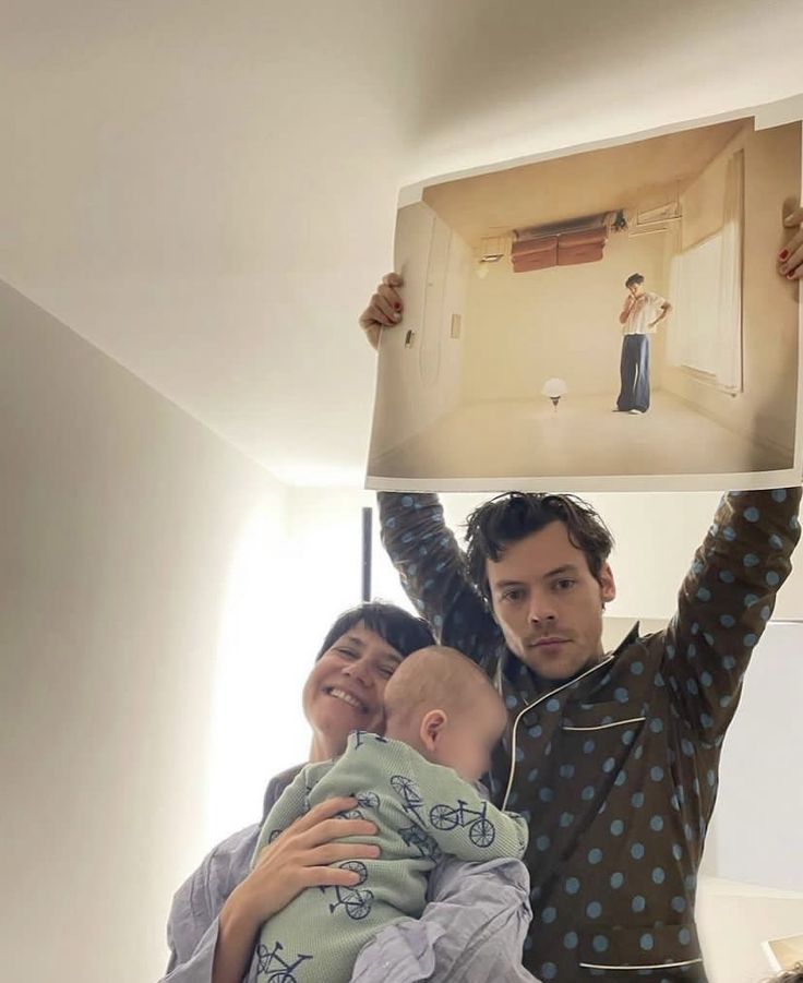 a man and woman holding a baby in front of their face with an image on the wall behind them