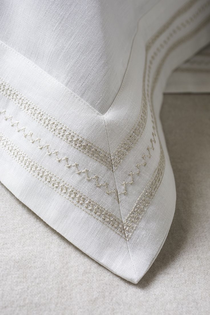 a close up view of a bed with white linens and embroidered trim on it