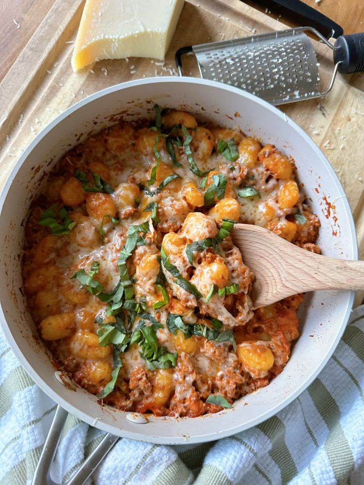 a wooden spoon is in a white bowl filled with pasta and cheese on a cutting board