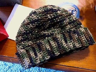 a knitted hat sitting on top of a wooden table next to a red bag